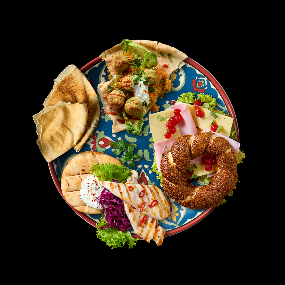 Orientalisch dekorierter Teller mit Falafel auf Fladenbrot, gegrillter Mini Pita mit Rotkraut und Hänchen sowie einem Sesamring mit Käse, Schinken und roten Johannisbeeren.
