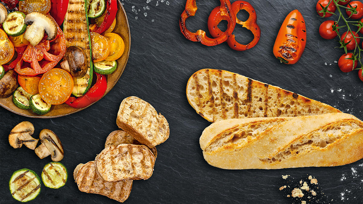 Grill-Baguettes im Hintergrund sind gegrillte Champignons, Tomaten, Paprika und Zucchini