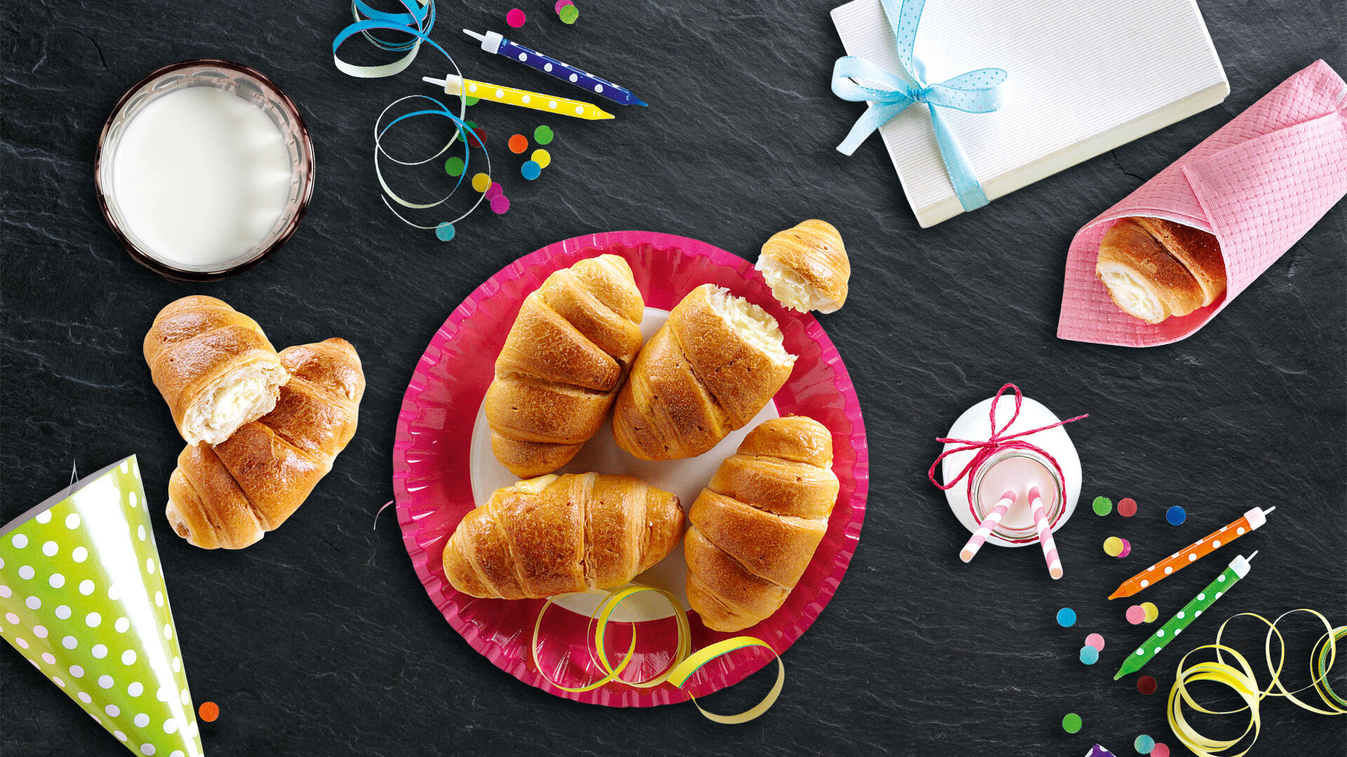 Kindercroissants auf pinkem Teller. Im Hintergrund sind Kerzen, Luftschlangen und Partyhütchen zu sehen.