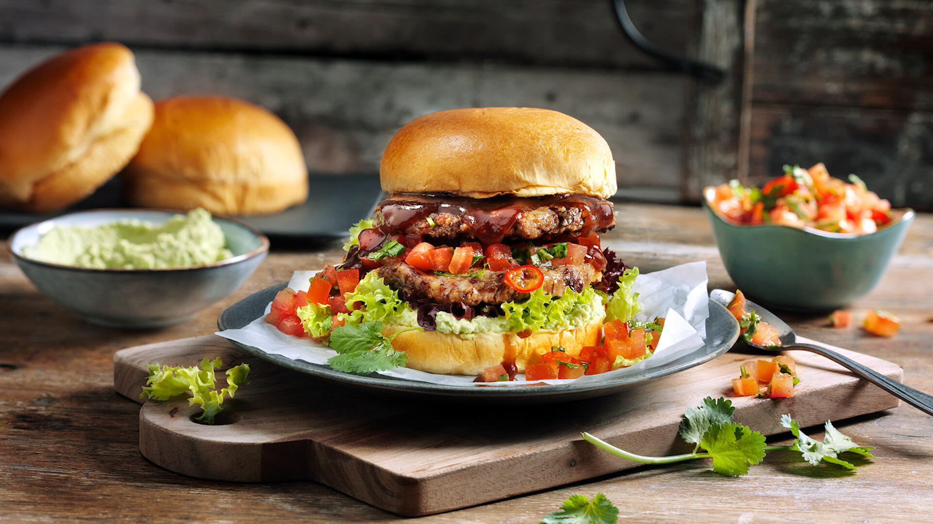 Belegter Brioche Burger auf einem Teller mit Salat in einer Schale