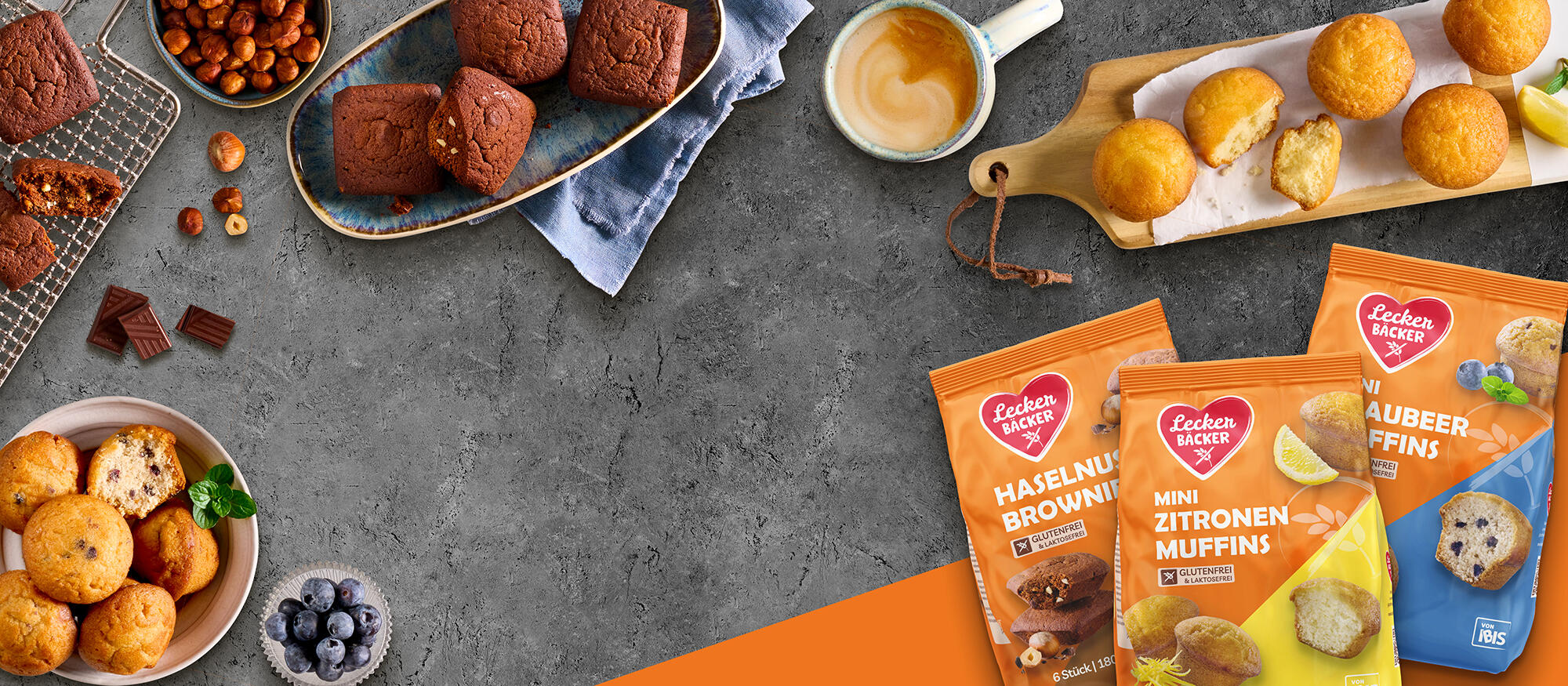 Schälchen und Teller mit Muffins und Brownies auf einem grauen Steinhintergrund.