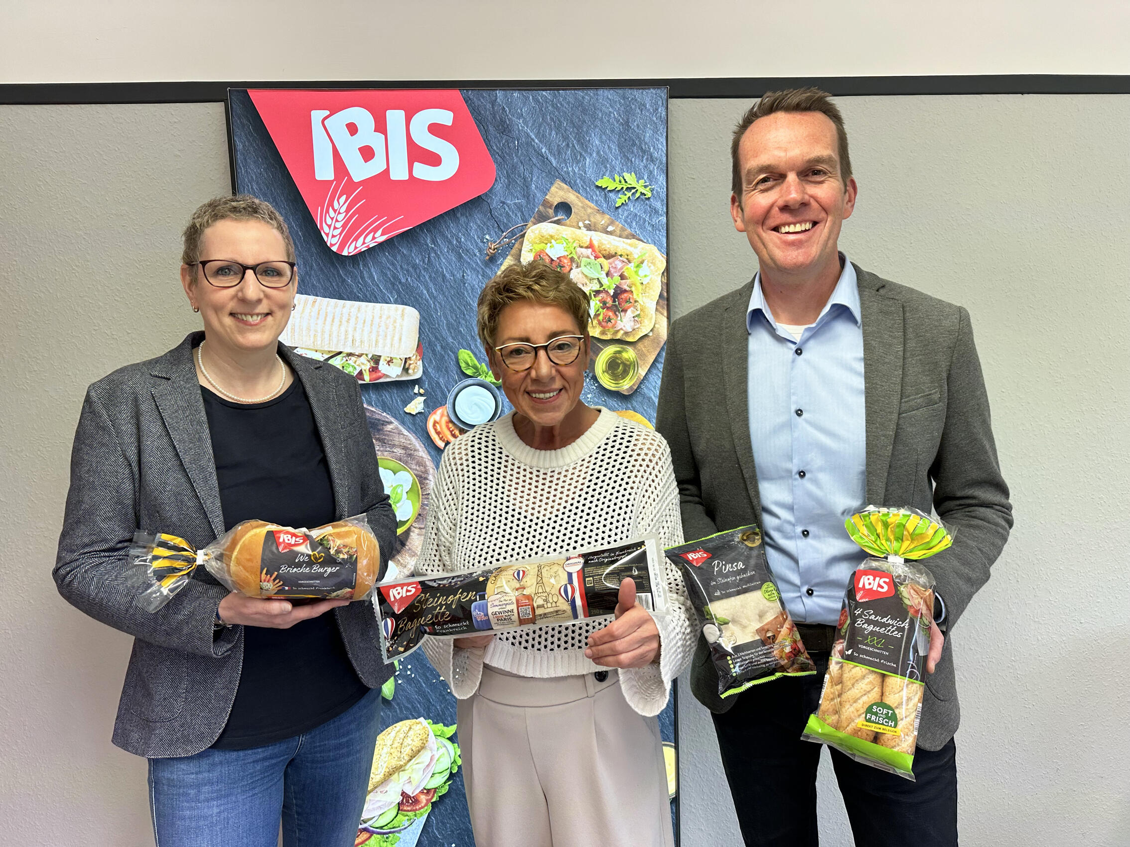 Drei IBIS Mitarbeiter, die vor einem IBIS Logo Produkte in die Kamera halten